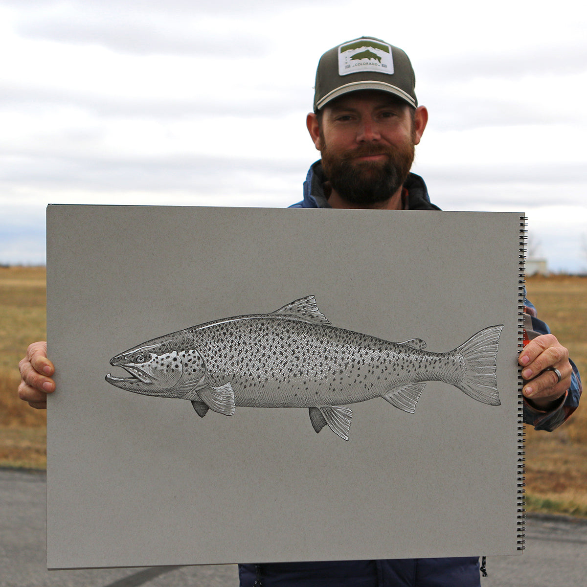 A man holds up a black and white drawing of a brown trout